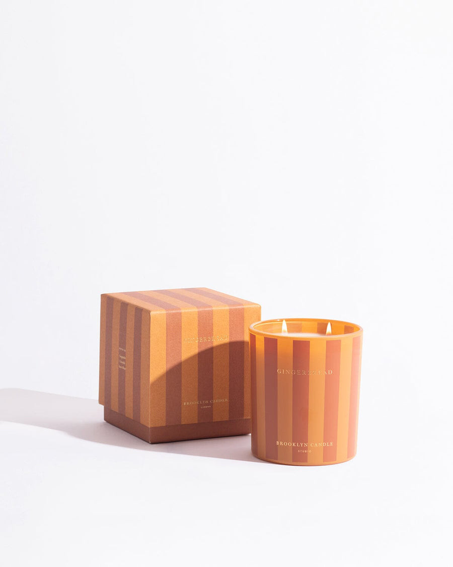 A gingerbread candle by Brooklyn Candle Studio, lit, on a dark ground