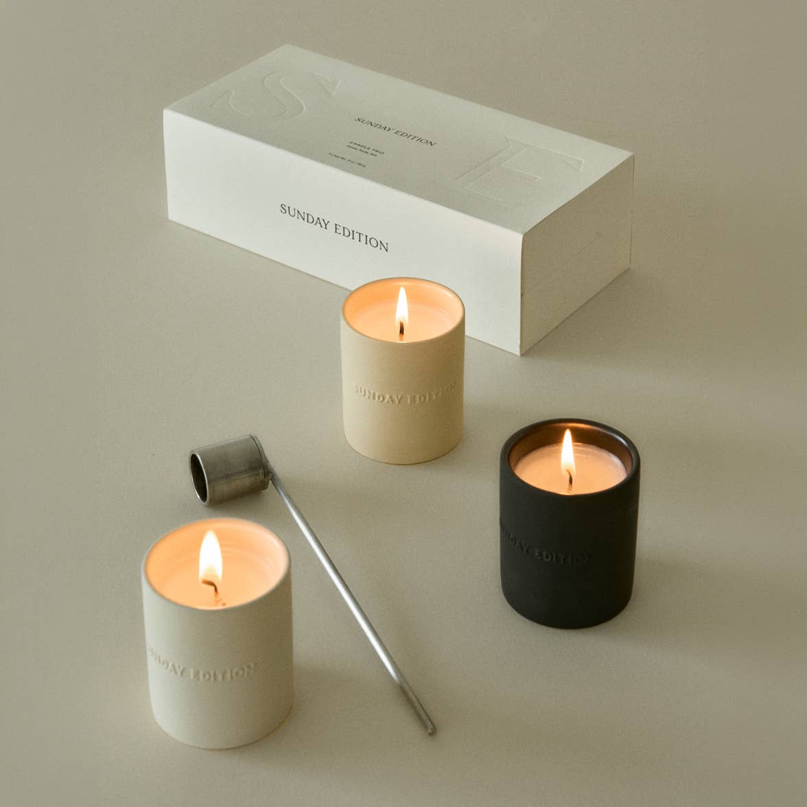 Two Sunday Edition candles lit, with a wick snuffer