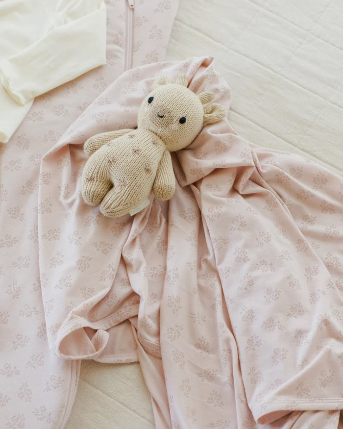 A pink floral sleep set and a knit bunny lovey, laid out on a bed