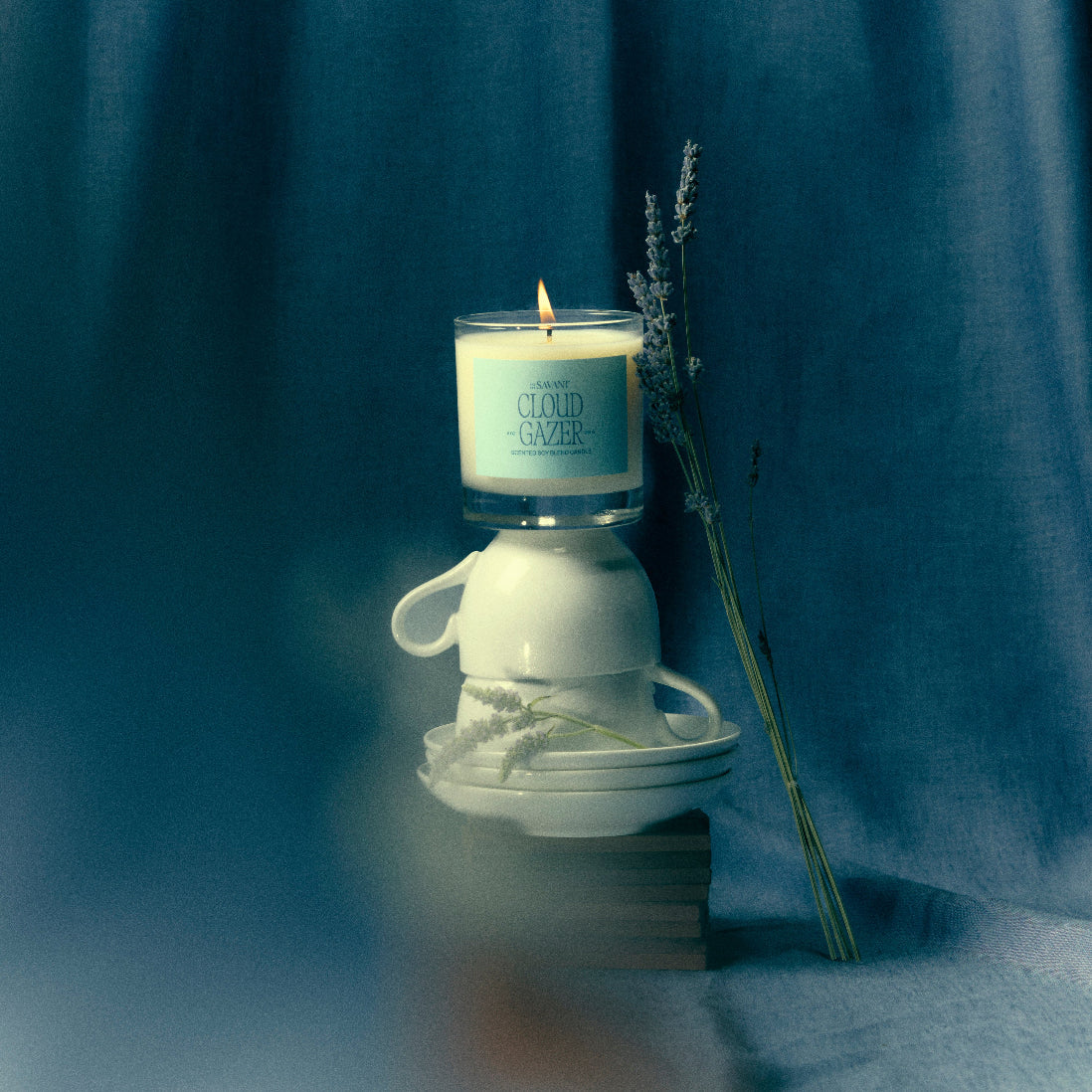 The New Savant Cloud Gazer Candle lit on a stack of teacups with lavender