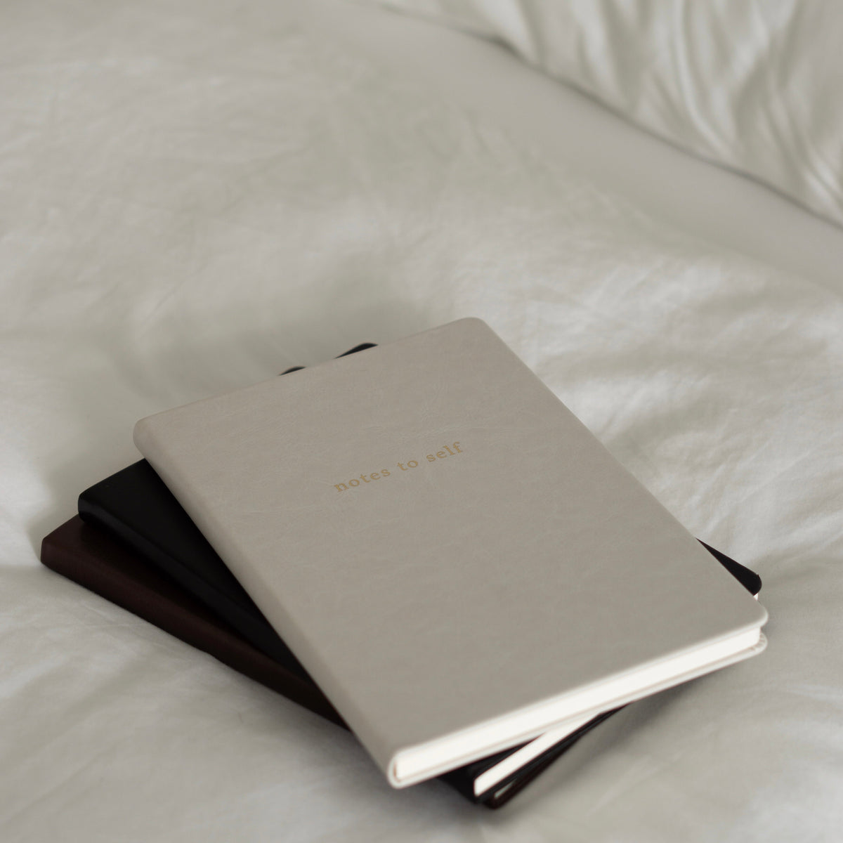 Notes to Self lined journal in beige, stacked on a bed