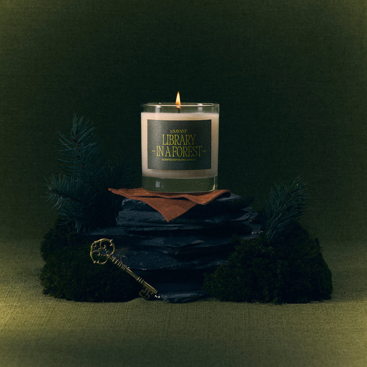 The New Savant Library in a Forest Candle on slate with moss and a brass key