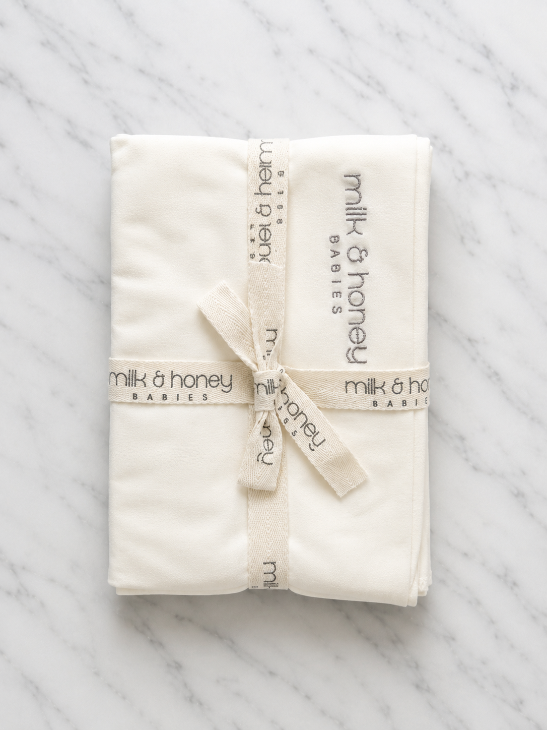 The Organic Swaddle folded and tied with milk and honey babies ribbon, undyed ivory organic cotton